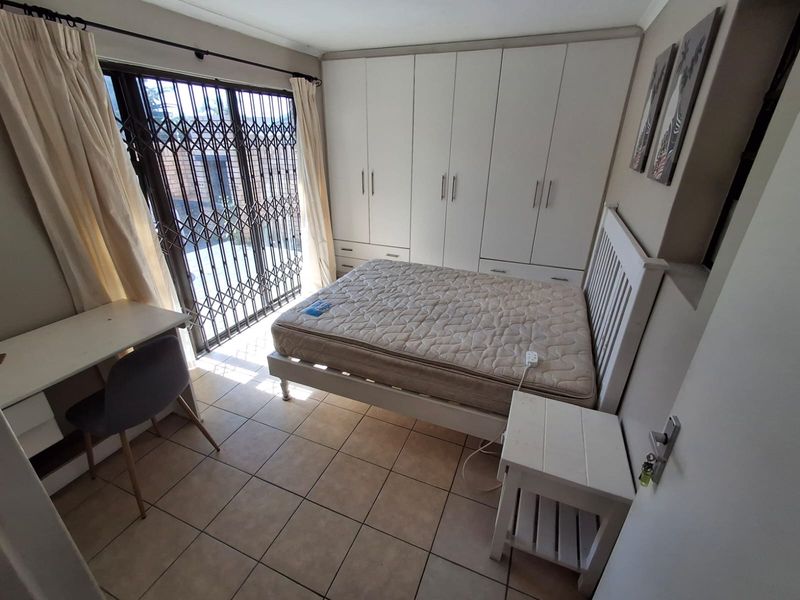A bedroom featuring built-in cupboards, tiled flooring, and a sliding door with a security gate leading to the exterior.