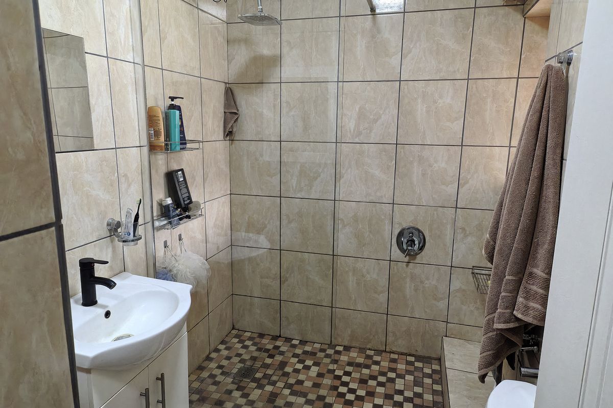 A functional bathroom featuring a vanity basin with a modern black faucet, a walk-in shower with a glass screen, and neutral wall tiling.