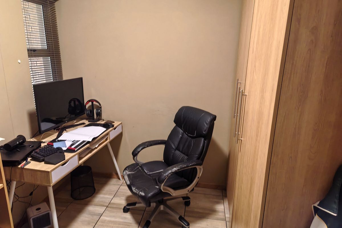 A compact bedroom featuring tiled flooring, a built-in wardrobe, and a window with venetian blinds.