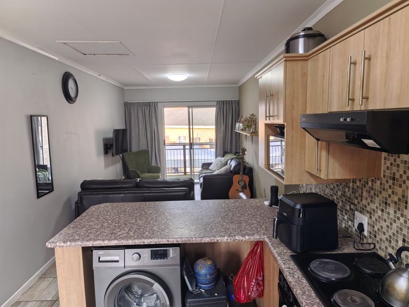 Open-plan living area featuring a compact kitchen with laminate cabinetry, mosaic backsplash, and integrated appliances, flowing into a lounge with balcony access.