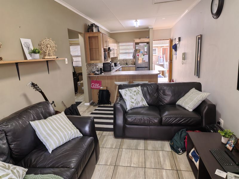 Open-plan living area featuring a functional kitchen with laminate countertops, mosaic backsplash, and tiled flooring throughout the combined space.