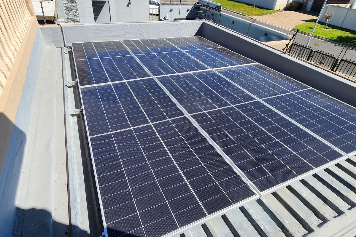 A high-angle view of a flat roof installation featuring a grid of solar panels, showing the property's energy infrastructure.
