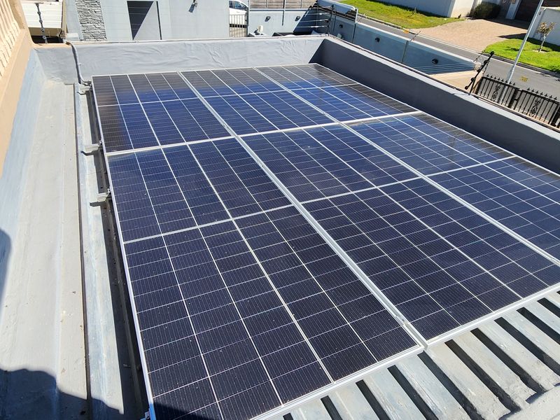 A high-angle view of a flat roof installation featuring a grid of solar panels, showing the property's energy infrastructure.