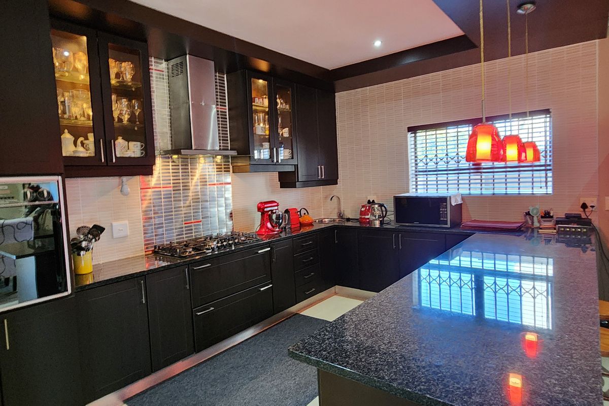 Modern kitchen featuring dark cabinetry, granite countertops, a central island, and a gas hob with a stainless steel extractor fan.