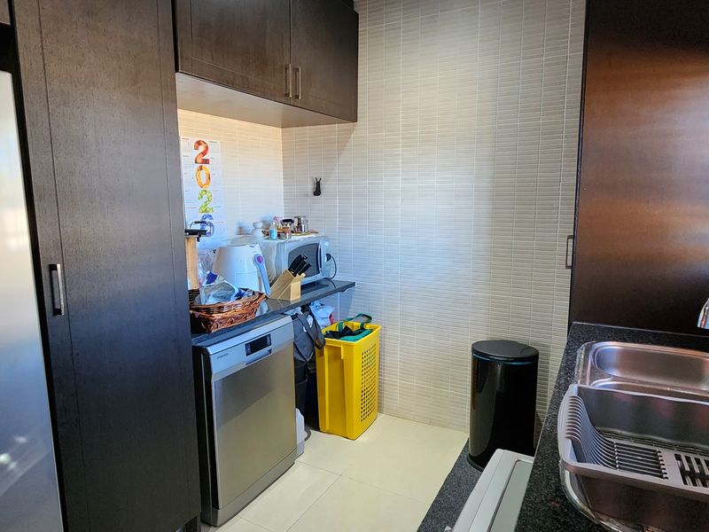 A functional scullery featuring dark built-in cabinetry, granite countertops, a double stainless steel sink, and tiled wall finishes.