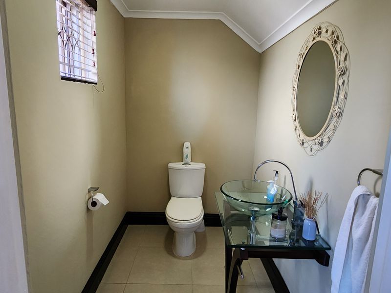 A compact guest bathroom featuring a modern glass vessel sink, chrome fixtures, and a standard toilet with neutral wall finishes.
