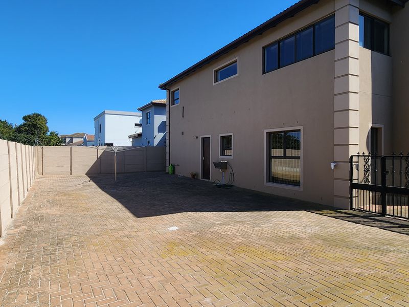 Spacious rear exterior area featuring paved surfacing, enclosed by a precast concrete boundary wall with a secure wrought iron gate.