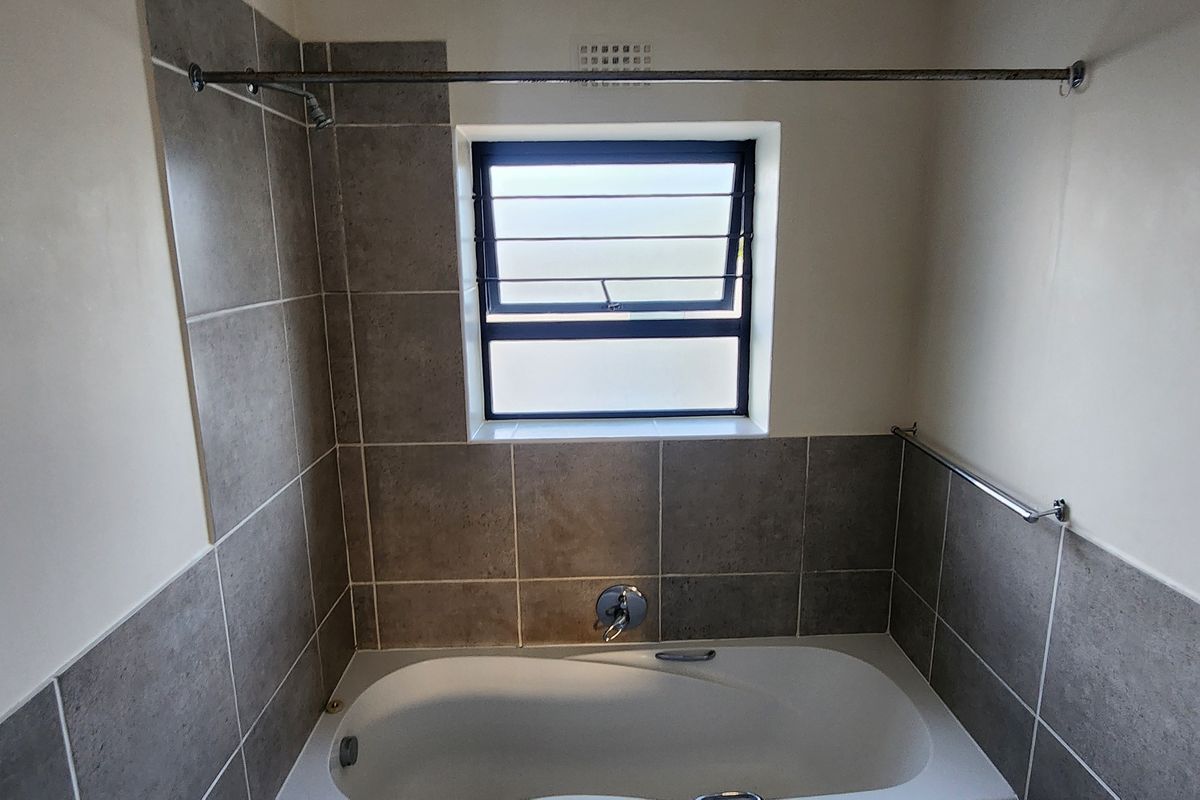 A clean, functional bathroom featuring a built-in bathtub with tiled surround, louver window for ventilation, and a chrome shower curtain rod.
