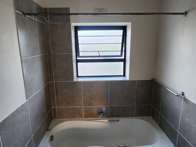 A clean, functional bathroom featuring a built-in bathtub with tiled surround, louver window for ventilation, and a chrome shower curtain rod.