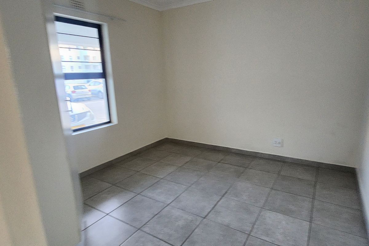 An empty bedroom featuring neutral walls, tiled flooring, and a window with security bars.