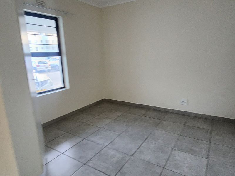 An empty bedroom featuring neutral walls, tiled flooring, and a window with security bars.