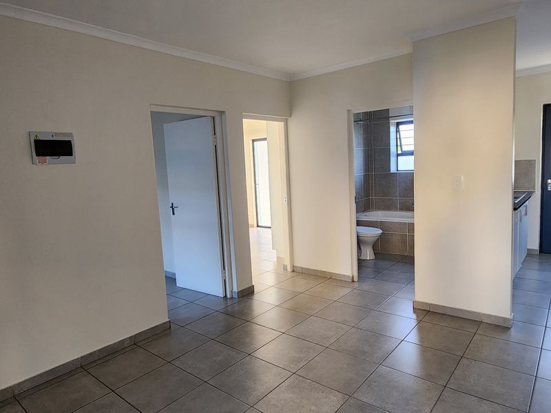 Open plan living area featuring tiled floors, leading to a kitchen with built-in appliances and access to a bathroom and additional rooms.