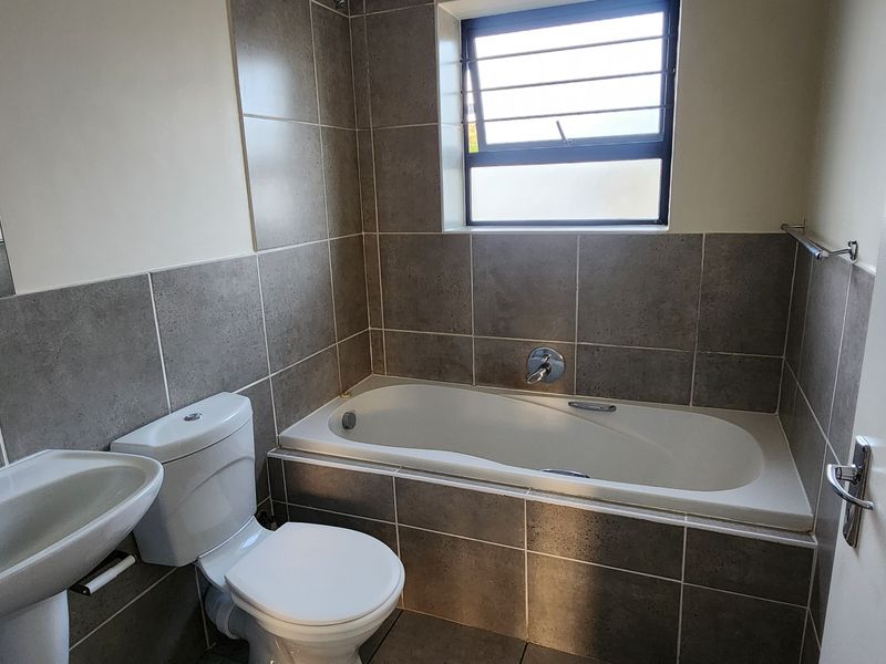 A clean, functional bathroom featuring a pedestal basin, toilet, and a built-in bathtub with neutral grey wall and floor tiling.