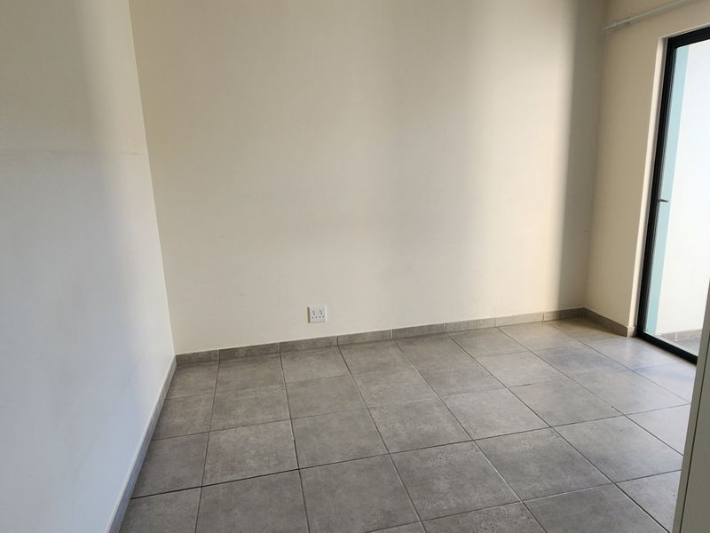 A clean, empty bedroom featuring neutral tiled flooring and a sliding glass door providing natural light.