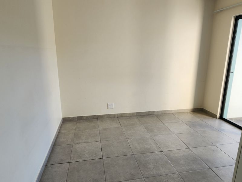 An empty bedroom featuring neutral tiled flooring, clean walls, and a glass door providing natural light.