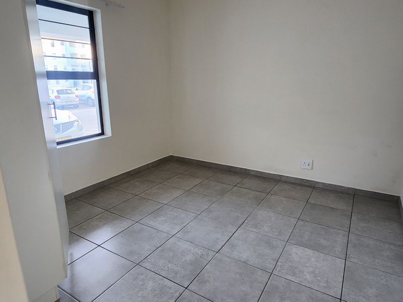 A clean, empty bedroom featuring neutral tiled flooring and a large window, providing a blank canvas for personalization.