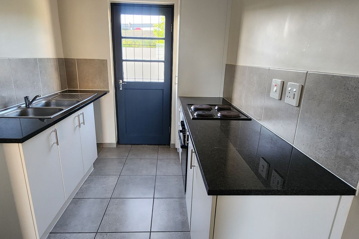 A clean, functional kitchen featuring white cabinetry, dark granite countertops, a built-in oven and hob, tiled backsplash, and direct access to the exterior.