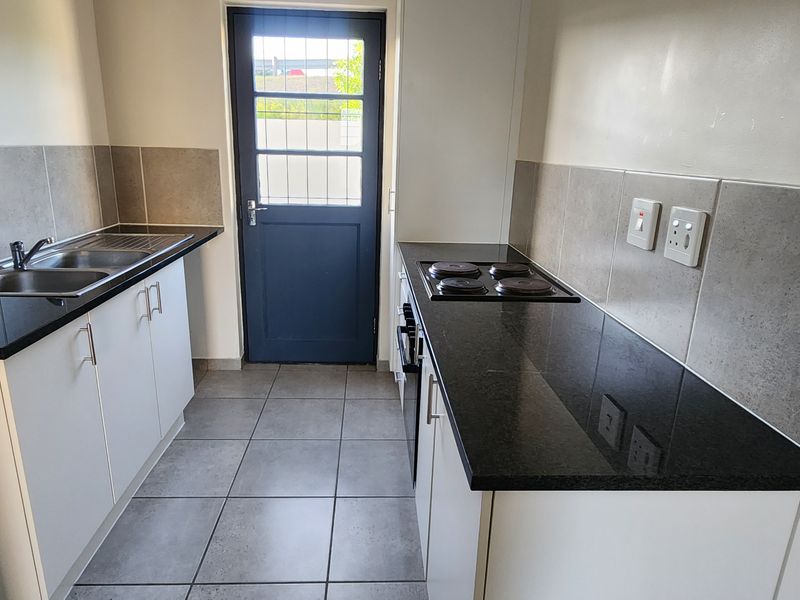A clean, functional kitchen featuring white cabinetry, dark granite countertops, a built-in oven and hob, tiled backsplash, and direct access to the exterior.