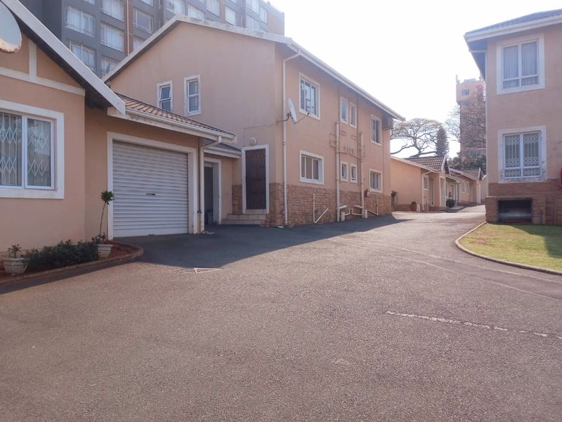 Exterior view of a townhouse complex featuring asphalt driveways, garage access, and traditional masonry and plaster finishes.