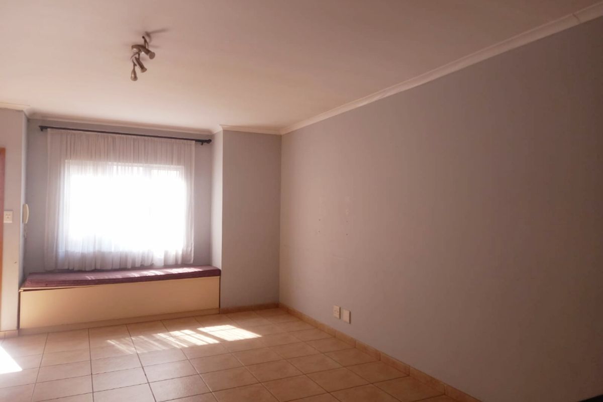 A bright, empty living room featuring ceramic floor tiles, a built-in window seat, and neutral wall finishes, offering a versatile space for customization.
