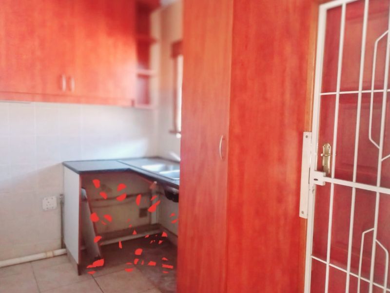 A dated kitchen area featuring wood-look cabinetry, a stainless steel sink, and tiled flooring, currently requiring repairs to the lower cabinet structure.