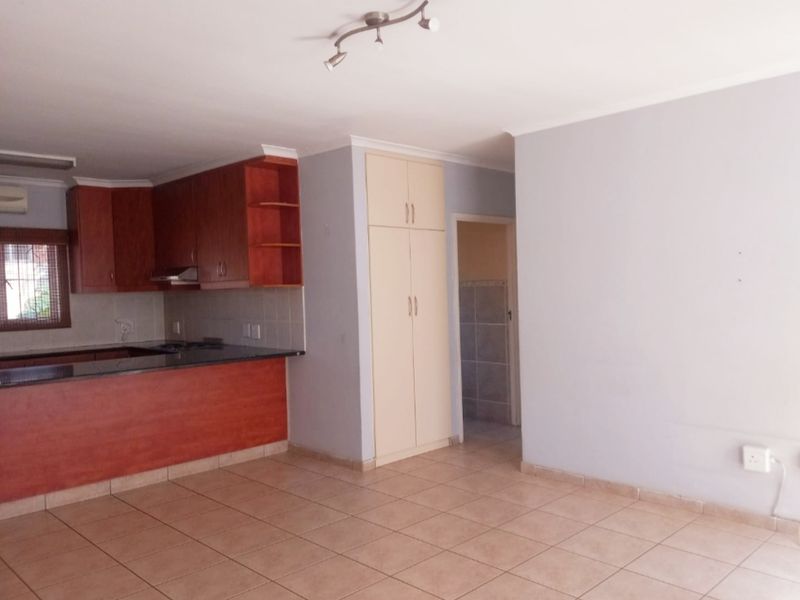 An open-plan kitchen and living area featuring tiled flooring, wooden cabinetry, granite countertops, and a built-in pantry cupboard.