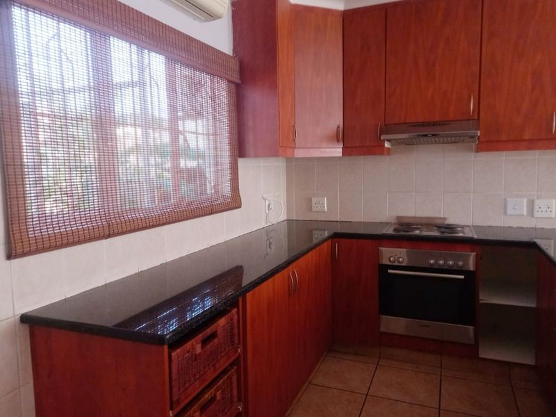 A functional kitchen featuring dark wood cabinetry, granite countertops, a built-in oven with hob, and a tiled backsplash.