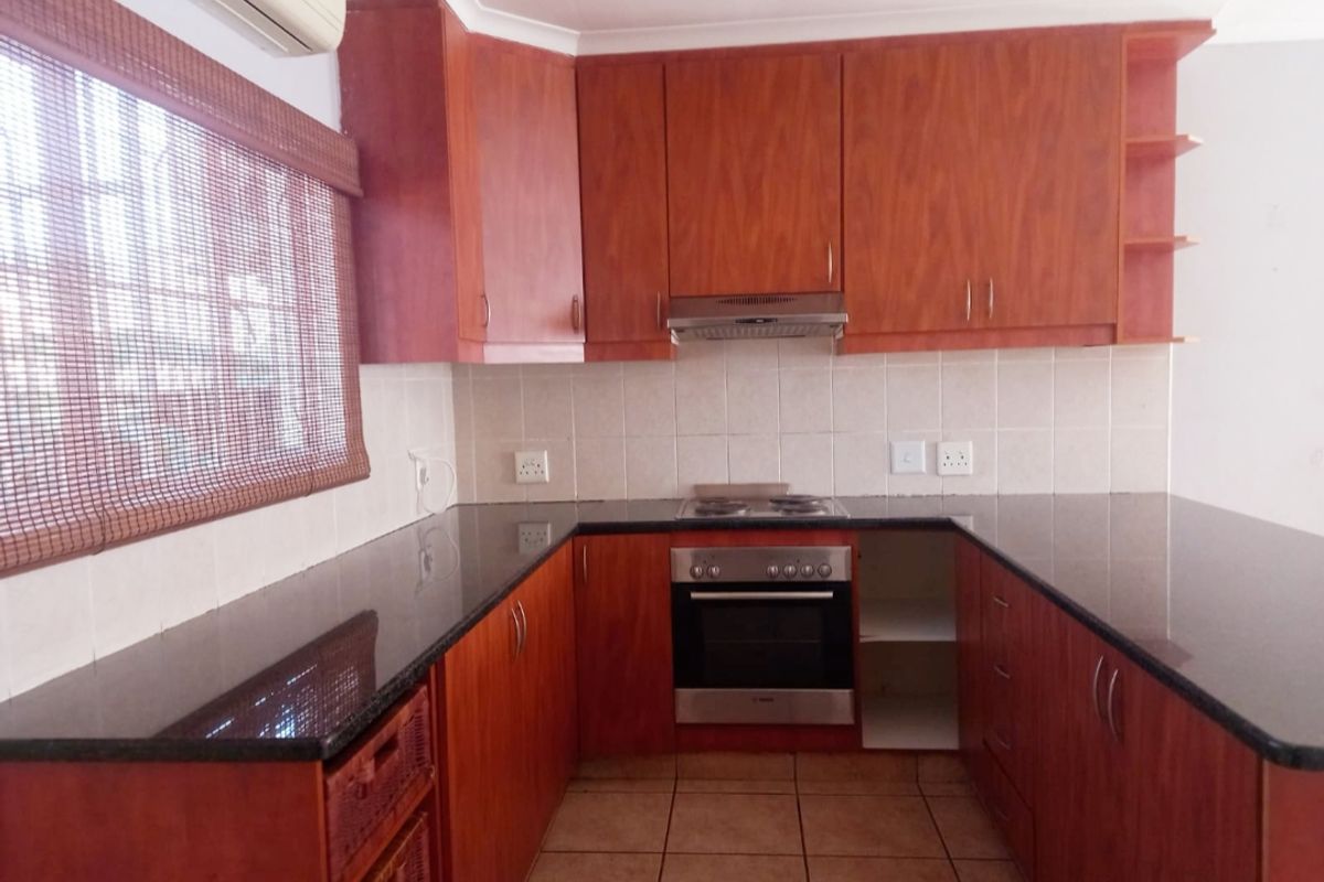 A functional kitchen featuring wood-finish cabinetry, granite countertops, built-in oven, hob, and extractor fan, with tiled flooring and backsplash.