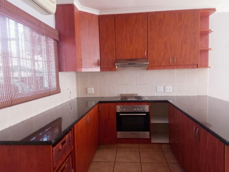 A functional kitchen featuring wood-finish cabinetry, granite countertops, built-in oven, hob, and extractor fan, with tiled flooring and backsplash.