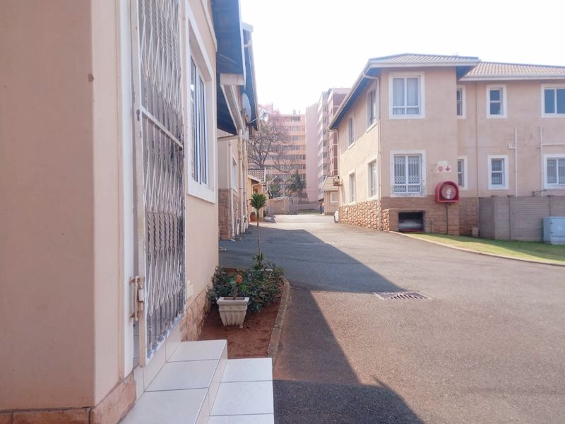 Exterior view of a townhouse complex featuring paved driveway access, security gates, and functional building infrastructure including fire safety equipment.