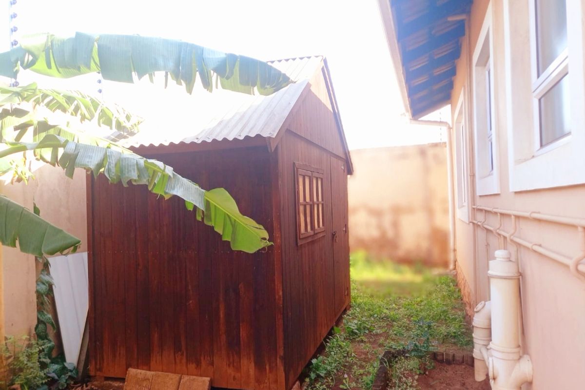A side yard view of a townhouse featuring a wooden garden shed, external plumbing infrastructure, and a boundary wall.