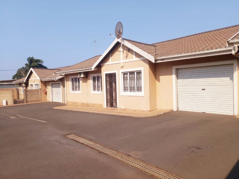 Front elevation of a townhouse featuring a tiled roof, roller garage door, security bars on windows, and a paved driveway.