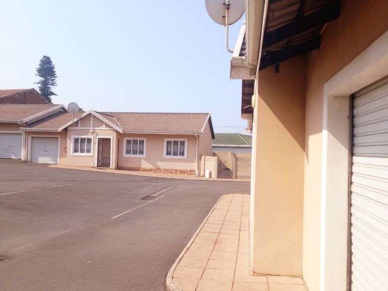 Exterior view of a townhouse complex featuring paved driveway access, garage doors, and tiled roof structures.
