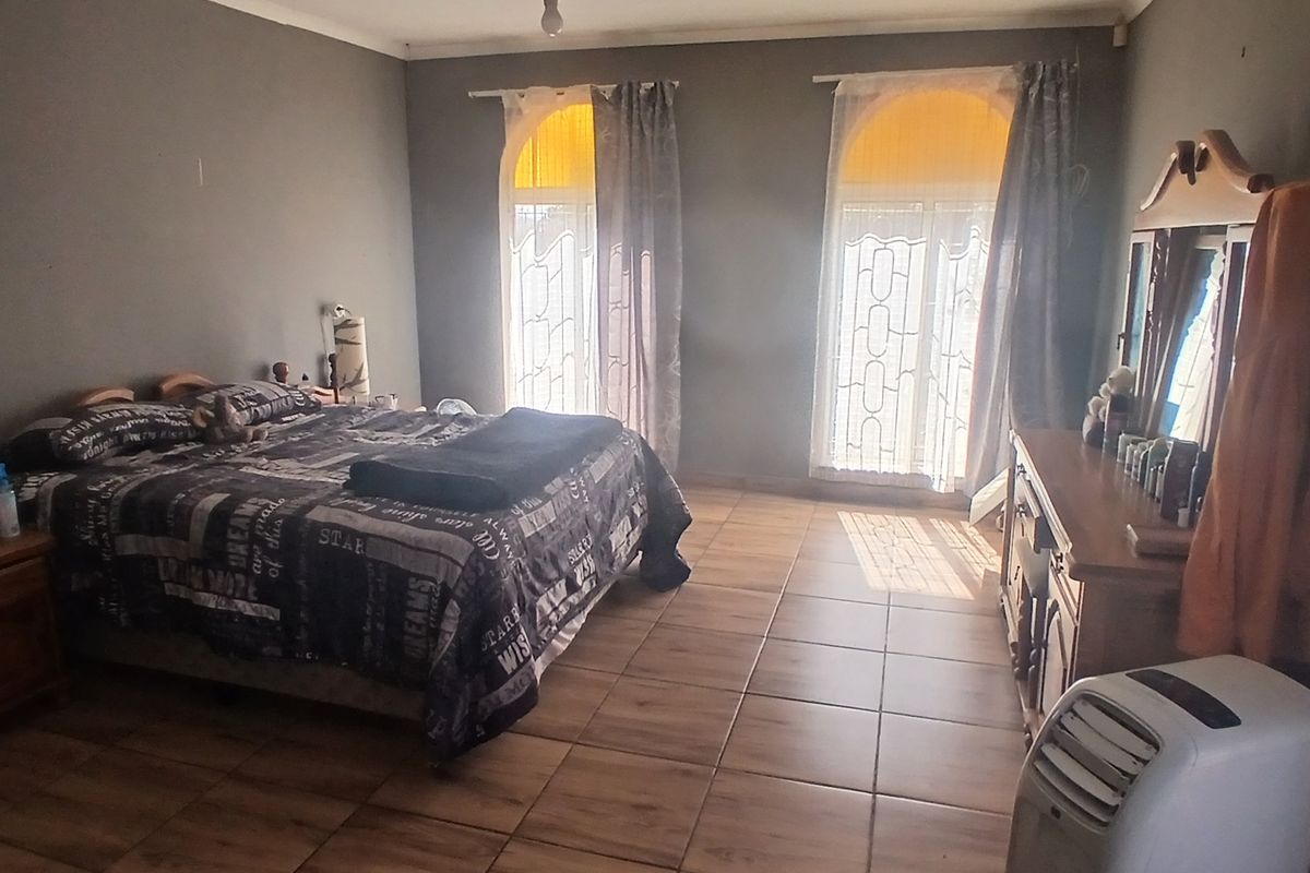 Spacious bedroom featuring wood-look tiled flooring, two arched windows allowing natural light, and neutral grey wall finishes.