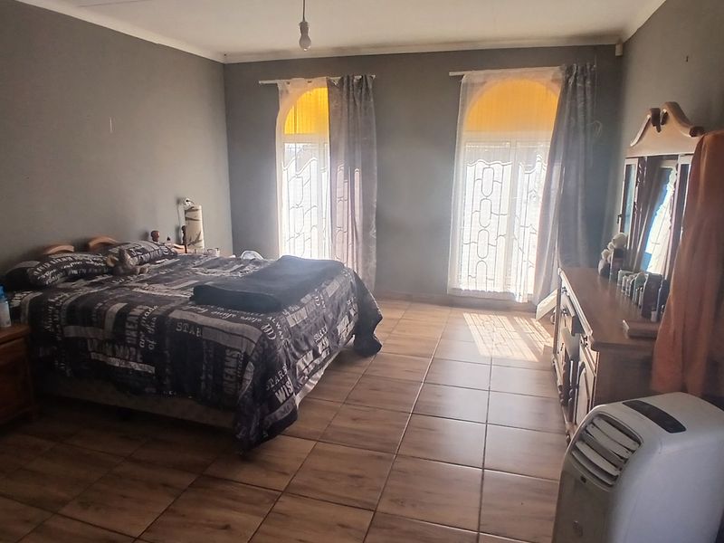 Spacious bedroom featuring wood-look tiled flooring, two arched windows allowing natural light, and neutral grey wall finishes.