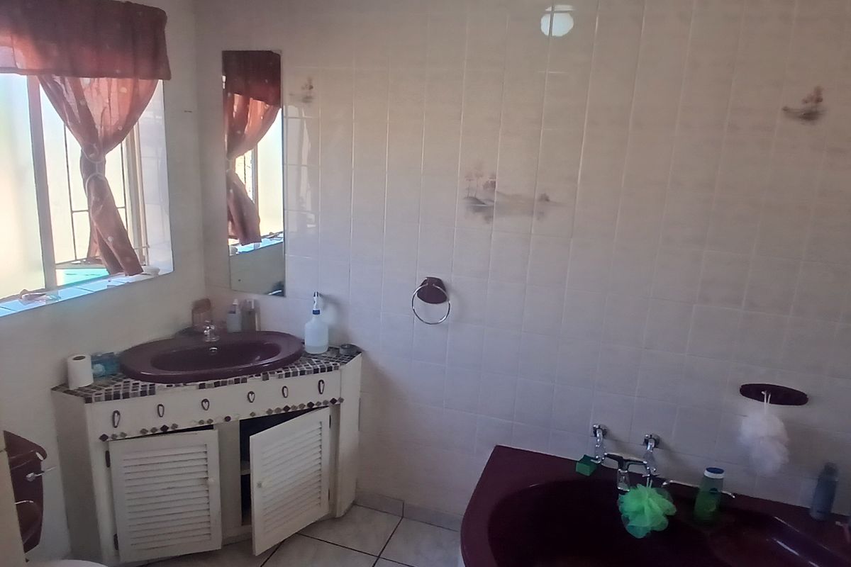 A dated bathroom featuring a corner bathtub, vanity cabinet with basin, and tiled finishes, currently showing signs of wear and ceiling water damage.