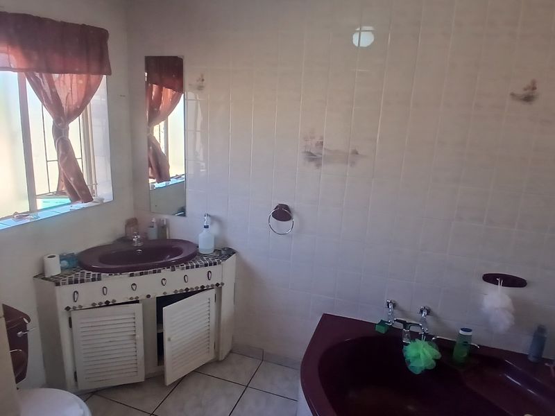 A dated bathroom featuring a corner bathtub, vanity cabinet with basin, and tiled finishes, currently showing signs of wear and ceiling water damage.