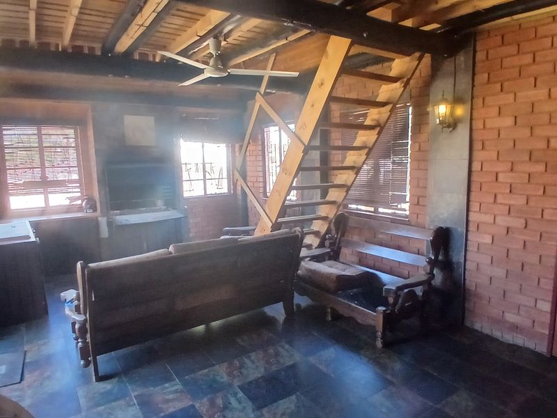Rustic living area featuring exposed brick walls, timber ceiling beams, slate flooring, and a built-in fireplace with an integrated timber staircase.