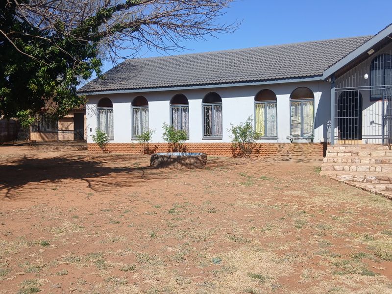 Rear view of a single-story house featuring a tiled roof, arched windows with security bars, and stone steps leading to the entrance.