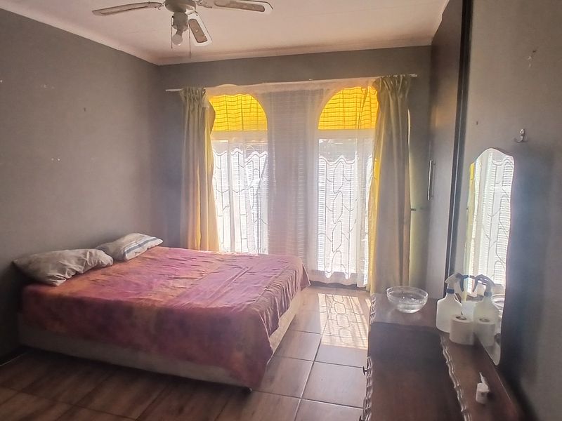 A bedroom featuring tiled flooring, a ceiling fan, and arched windows with natural light, providing a functional space with potential for cosmetic updates.