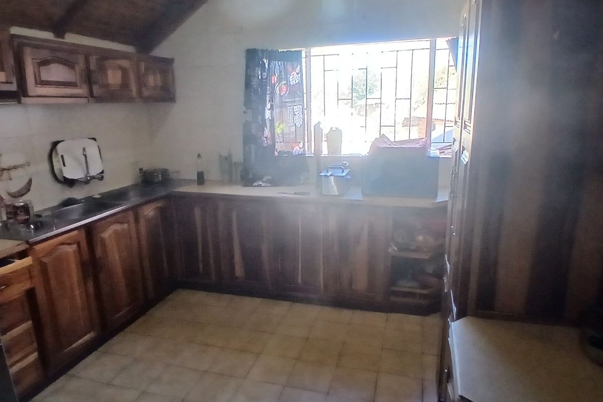 A dated kitchen featuring wooden cabinetry, tiled flooring, and a vaulted timber ceiling, requiring modernization to improve its aesthetic appeal and functionality.