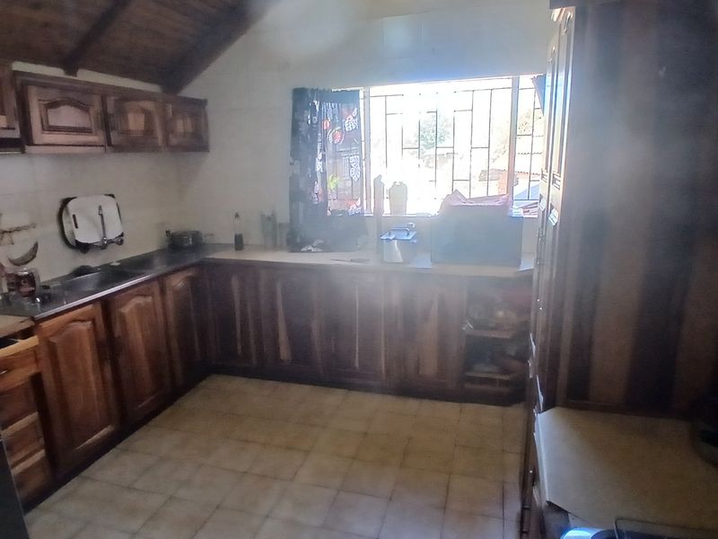 A dated kitchen featuring wooden cabinetry, tiled flooring, and a vaulted timber ceiling, requiring modernization to improve its aesthetic appeal and functionality.