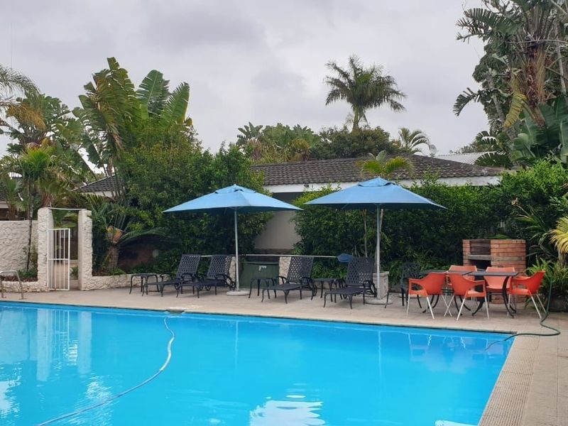 Outdoor pool area featuring a swimming pool, paved deck, and a built-in brick braai, surrounded by established garden landscaping.