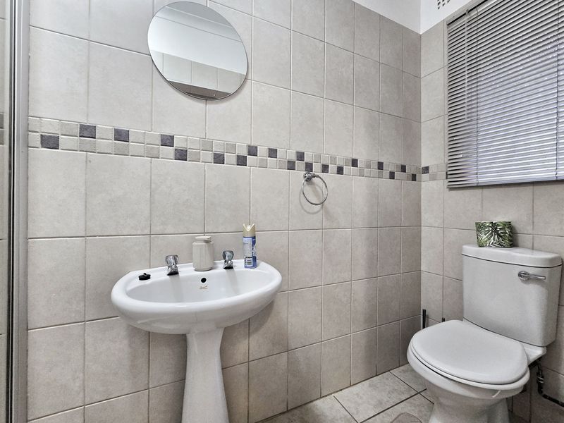 A functional bathroom featuring tiled walls with a decorative border, a pedestal basin, and a standard toilet.