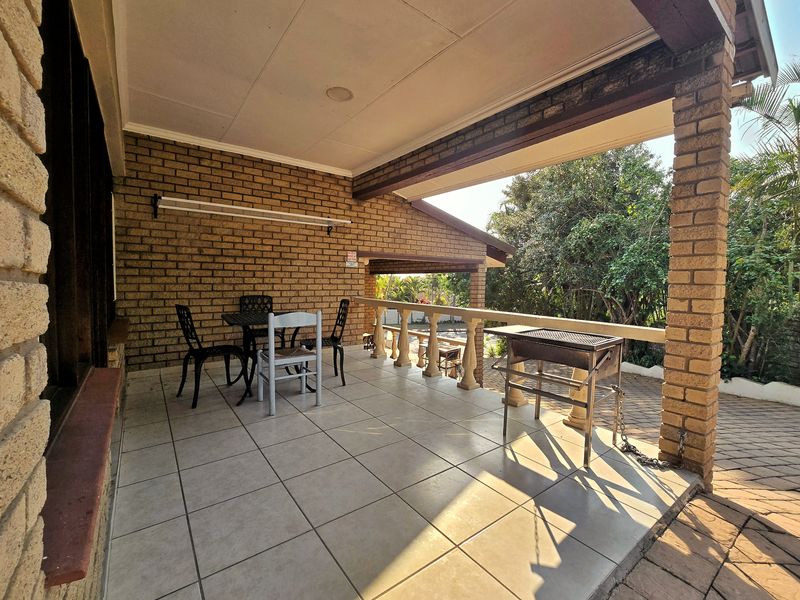 A spacious covered patio featuring tiled flooring, brick structural pillars, and a balustrade, offering an ideal outdoor space for relaxation and entertaining.