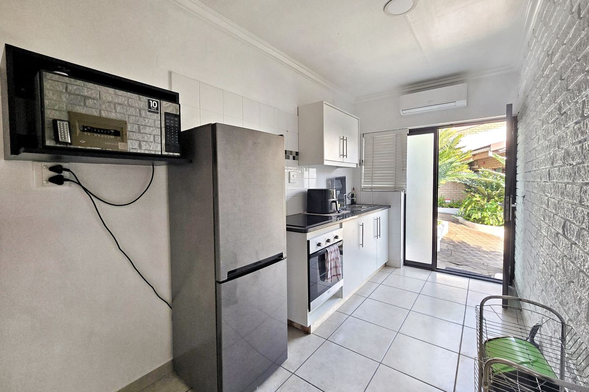 Compact kitchen featuring built-in cabinetry, oven, hob, and tiled flooring, with direct access to an outdoor patio area.