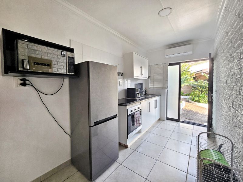 Compact kitchen featuring built-in cabinetry, oven, hob, and tiled flooring, with direct access to an outdoor patio area.