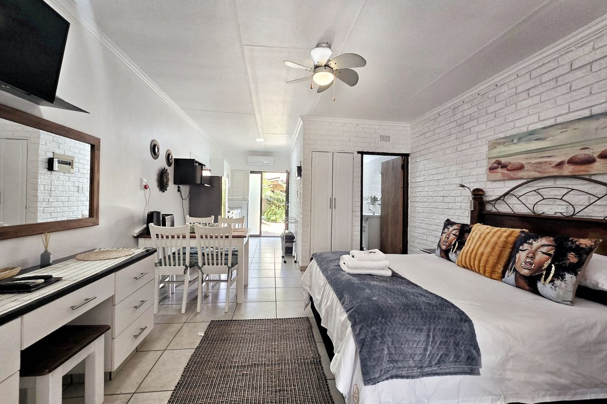 Open-plan studio apartment featuring tiled flooring, exposed brick feature wall, ceiling fan, and built-in storage, with direct access to an outdoor area.