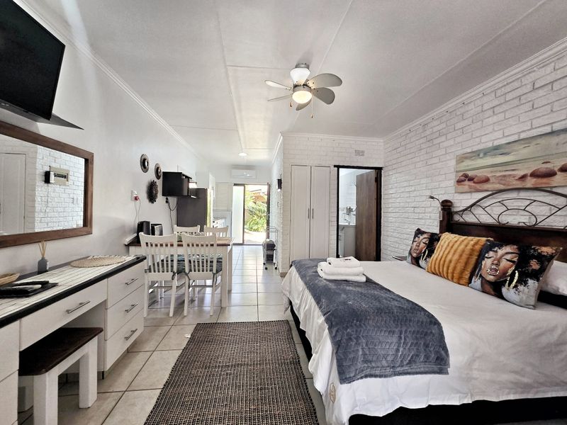 Open-plan studio apartment featuring tiled flooring, exposed brick feature wall, ceiling fan, and built-in storage, with direct access to an outdoor area.