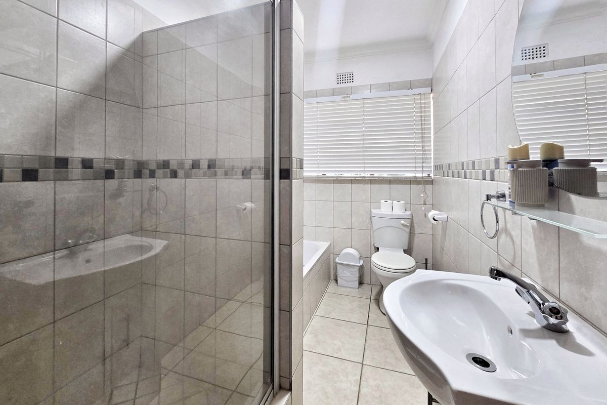 A well-maintained bathroom featuring a glass shower enclosure, a built-in bathtub, a pedestal washbasin, and neutral ceramic tiling throughout.